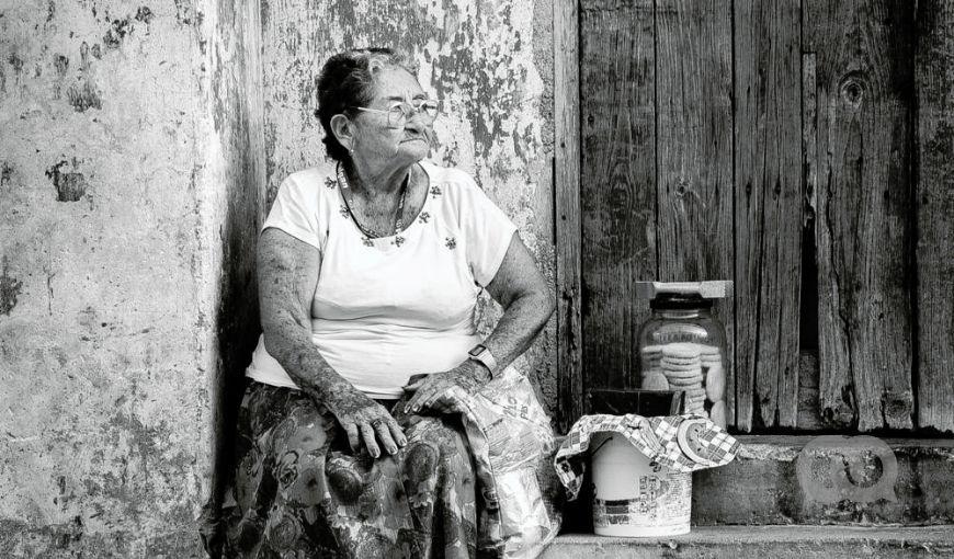 Mujer mayor sentada en la entrada de una casa, con productos caseros que vende para. Personas mayores