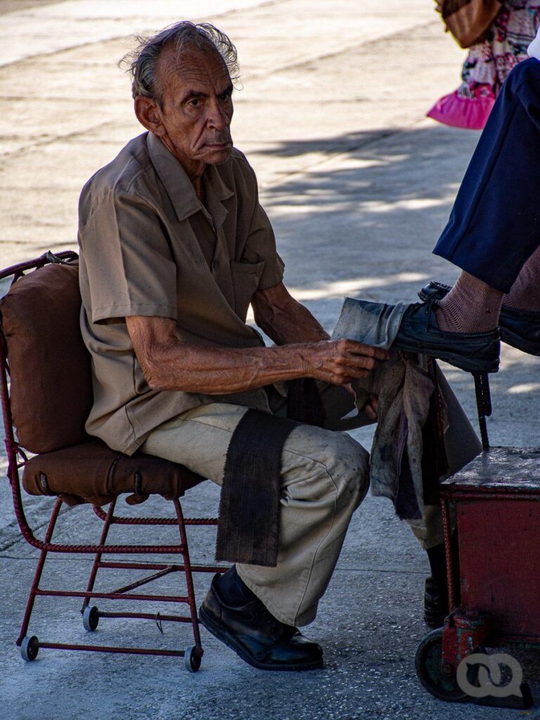 Hombre mayor en La Habana cuyo oficio es limpiador de zapatos, limpia los zapatos de un cliente