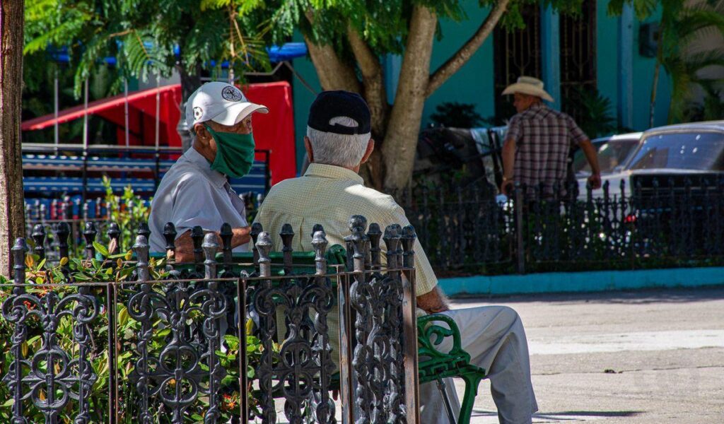 Dos personas mayores en un parque de Cuba, conversan bajo la sombra de un árbol