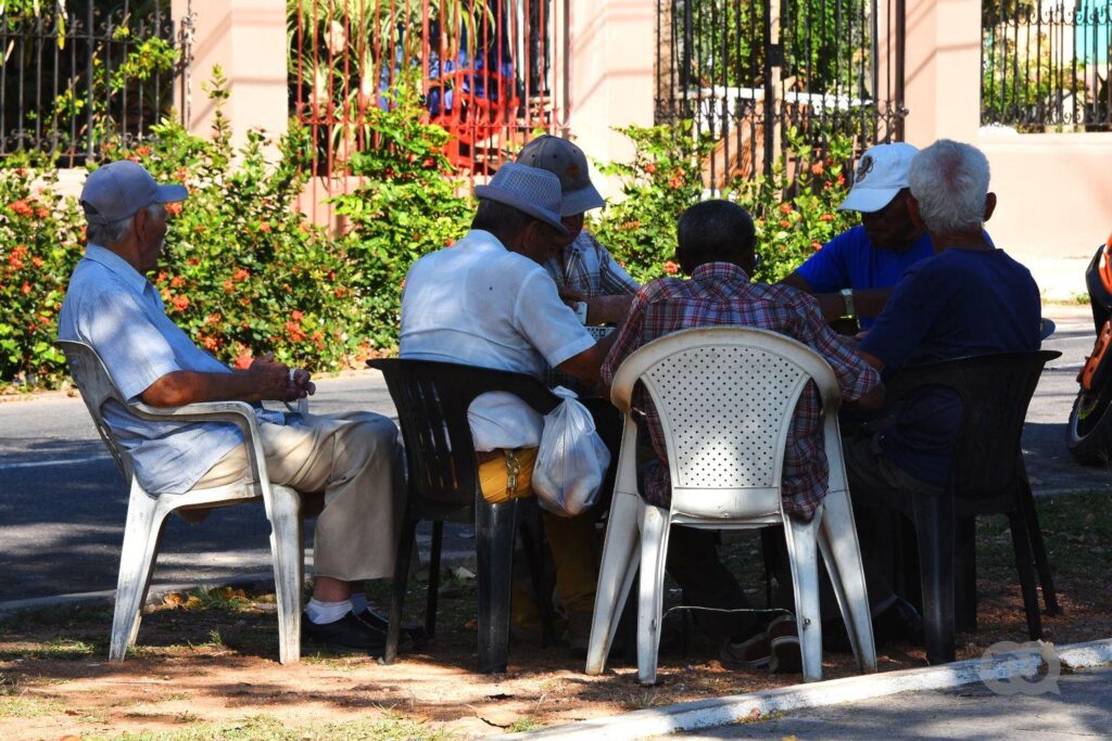 Grupo de personas mayores en La habana jugando dominó en un parterre 