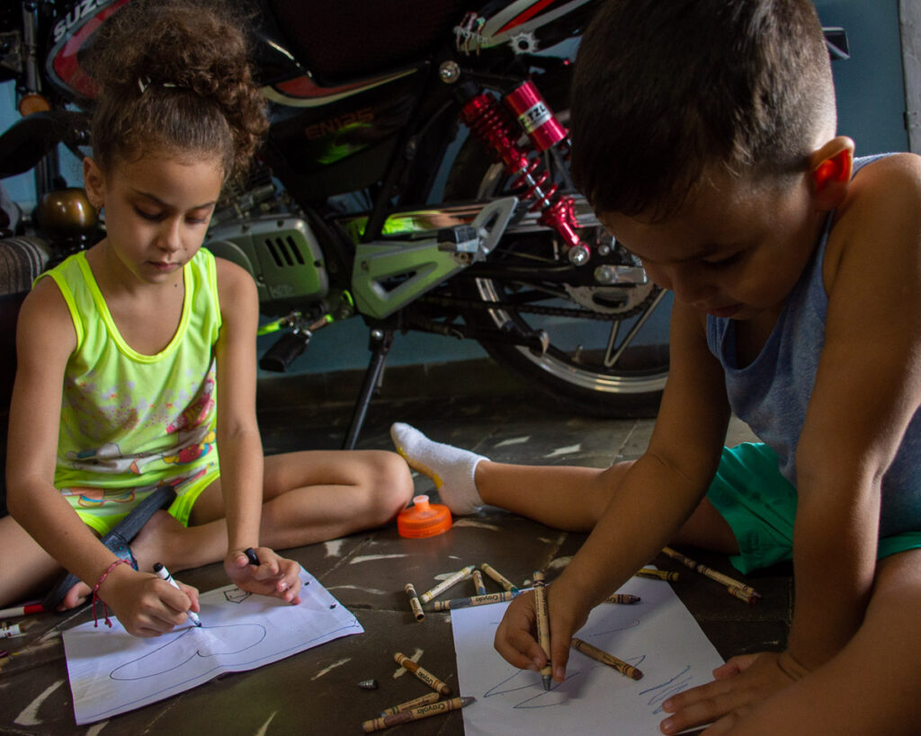 Una niña y un niño dibujan sentados en el piso. Salud mental para niños