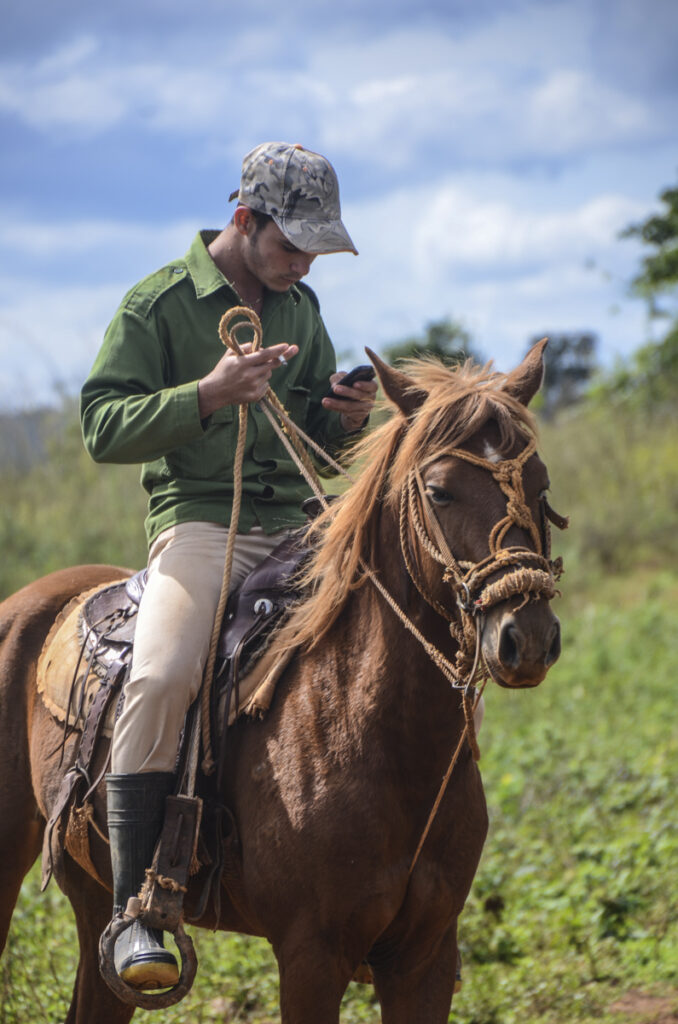 Campesino cubano monta caballo, mientra revisa su celular o móvil. Una forma de ser hombre en Cuba. 