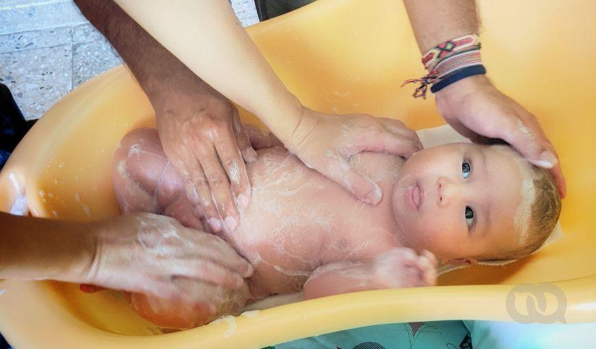 La madre y padre bañan a cuatro manos a su bebé en una palangana.