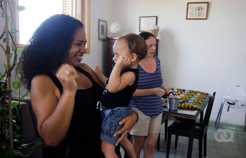 La familia formada por Dachelys y Hope en la sala de su casa, en su vida cotidiana. Una de las madres juega con su bebé. Es el primer bebé con dos madres reconocido en Cuba. (Madre)