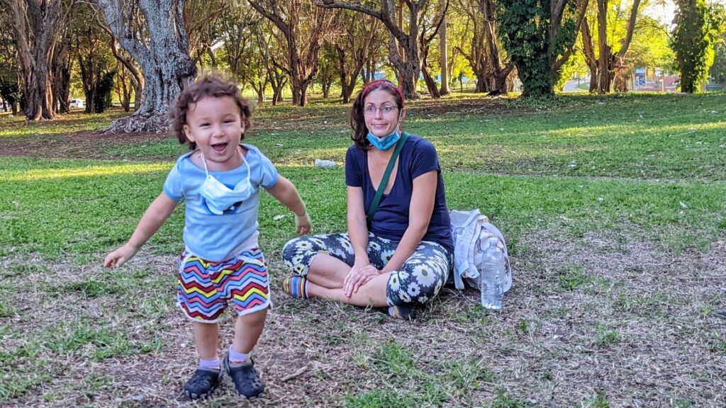 Madre sentada en la yerba mira a bebé sonriente en un parque La Habana Cuba