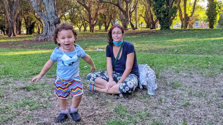 Madre sentada en la yerba mira a bebé sonriente en un parque La Habana Cuba